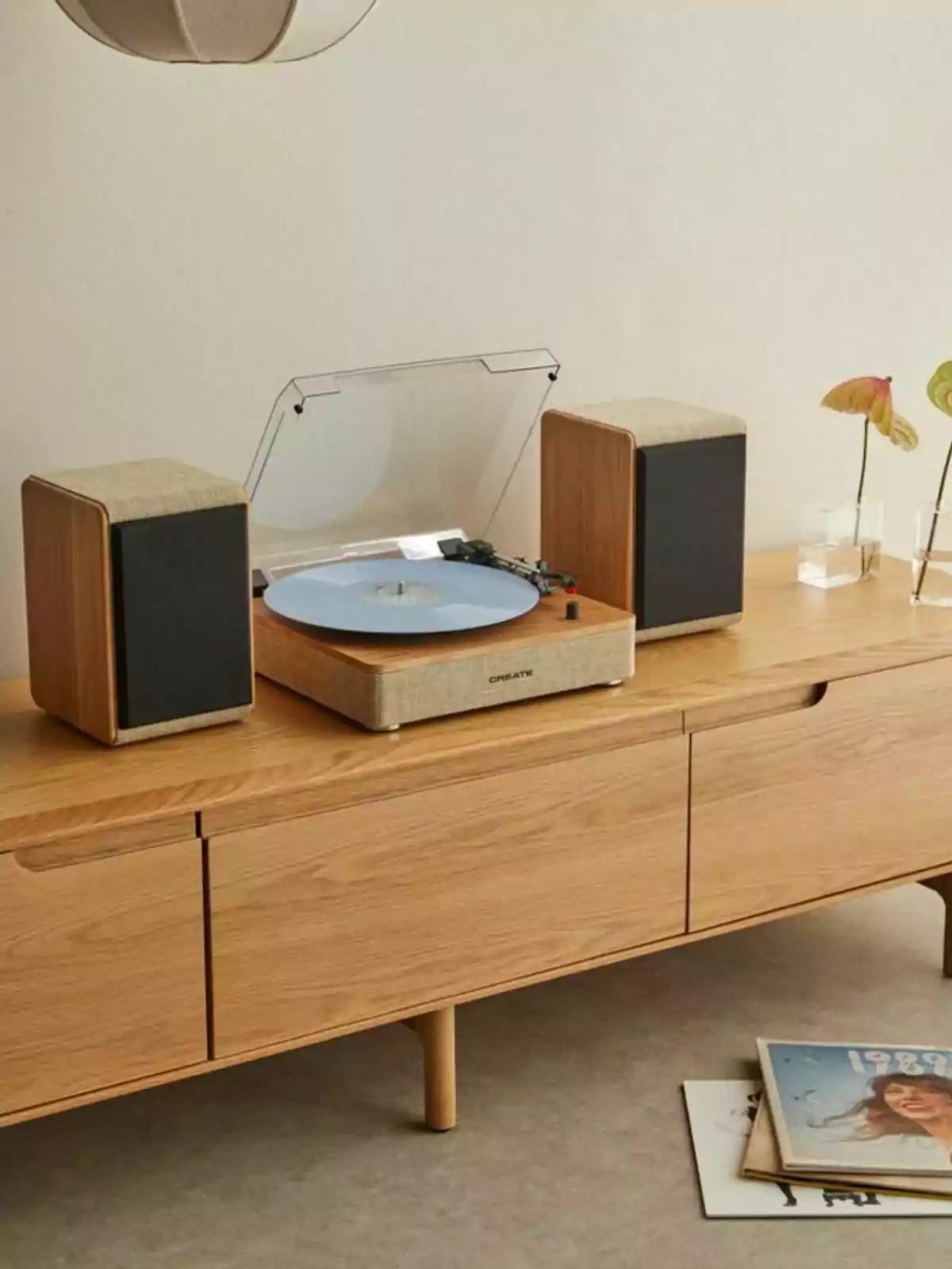 Un tocadiscos con un disco azul y dos altavoces sobre un mueble de madera clara con revistas en el suelo.