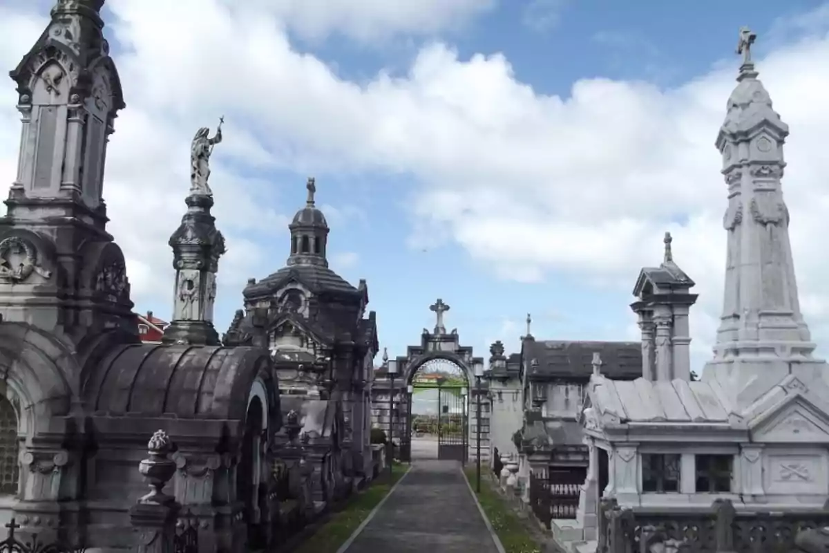 Vista de un cementerio con mausoleos ornamentados y estatuas bajo un cielo parcialmente nublado.