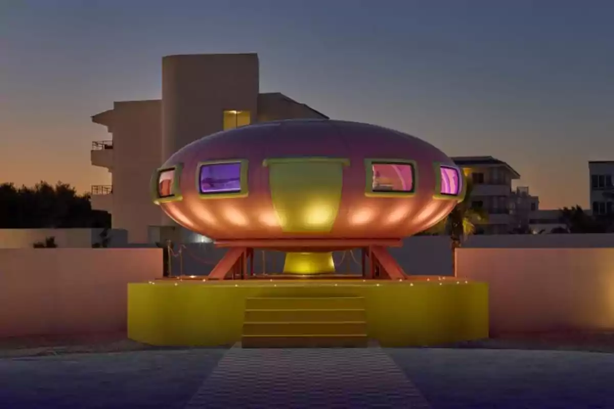 Casa futurista con forma de platillo volador iluminada por la noche.