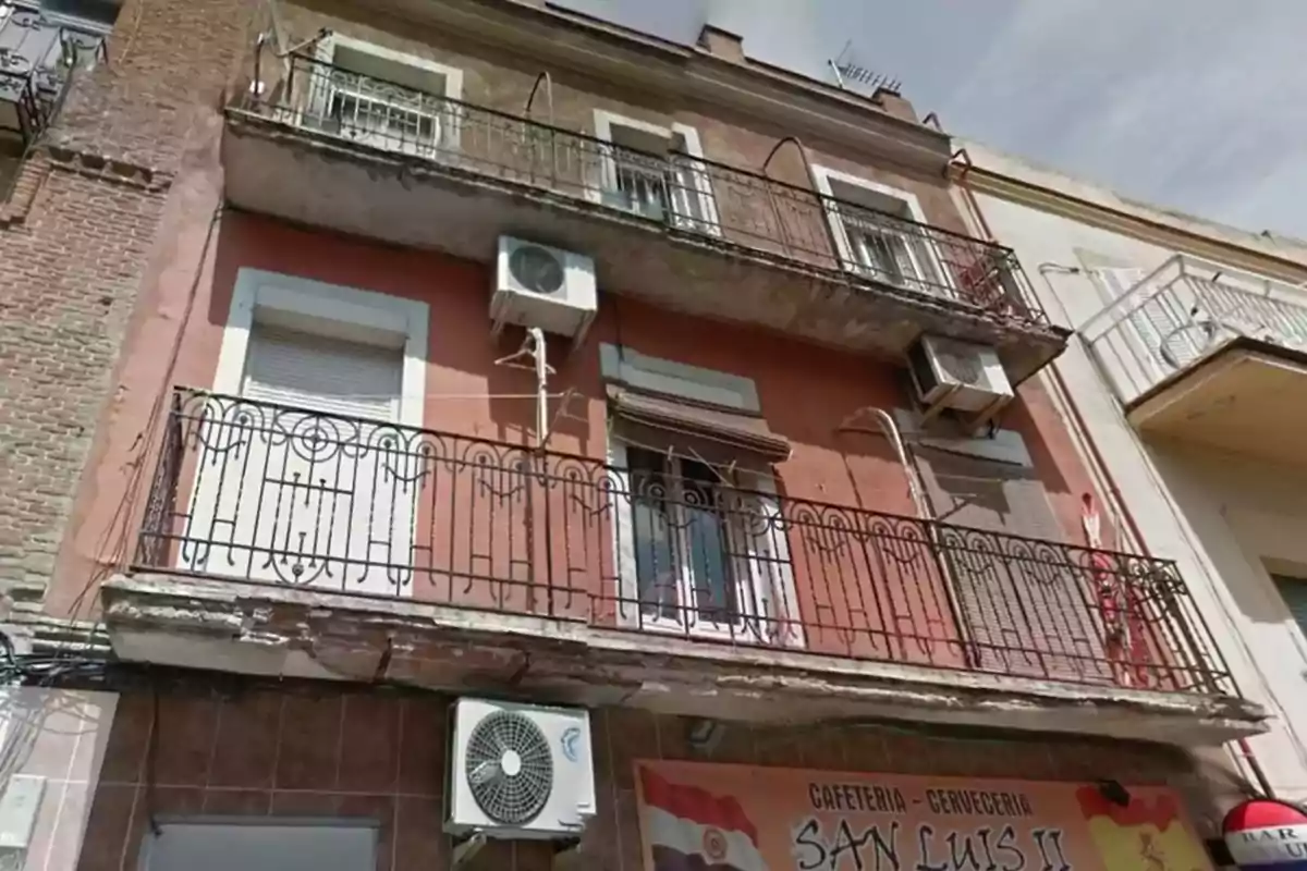 Fachada de un edificio antiguo con balcones de hierro forjado y unidades de aire acondicionado en la parte superior de una cafetería.