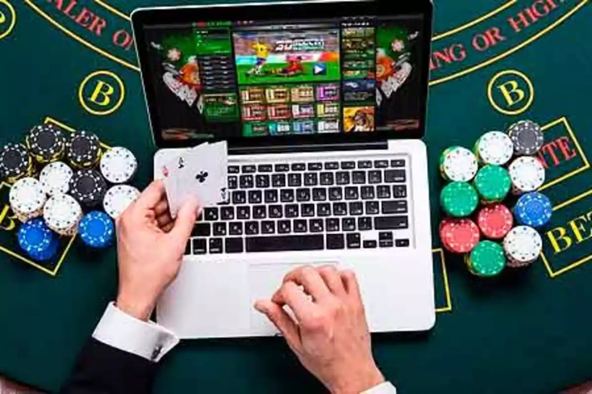 Persona jugando póker en línea en una computadora portátil con fichas de casino sobre una mesa verde