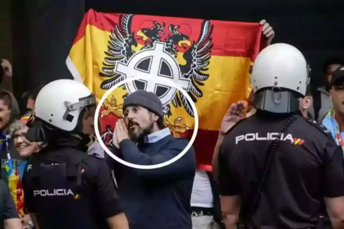 Un grupo de personas se encuentra frente a policías, uno de ellos sostiene una bandera con un símbolo en el centro.