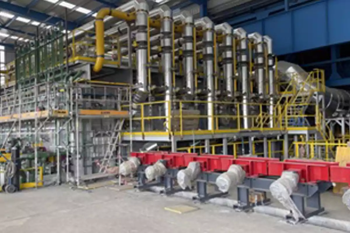 Vista de una maquinaria industrial grande con estructuras metálicas, tuberías amarillas y plataformas en el interior de una nave. Vista de una maquinaria industrial grande con estructuras metálicas, tuberías amarillas y plataformas en el interior de una nave.