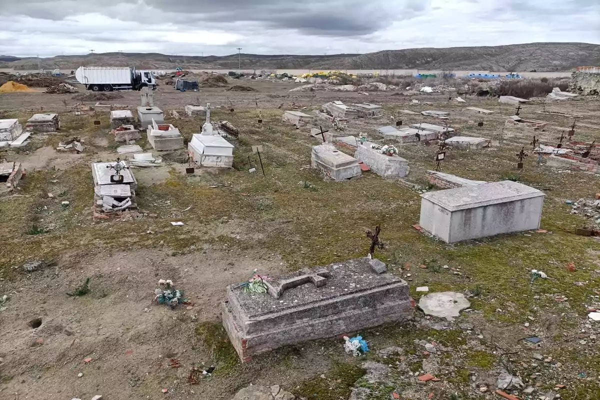 Un cementerio descuidado con tumbas deterioradas y un camión al fondo en un paisaje árido y nublado. Un cementerio descuidado con tumbas deterioradas y un camión al fondo en un paisaje árido y nublado.