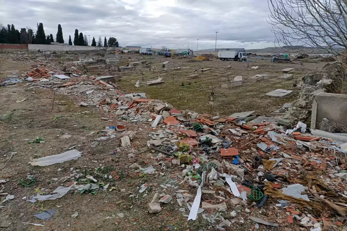 Un terreno lleno de escombros y basura con algunos árboles y camiones al fondo bajo un cielo nublado. Un terreno lleno de escombros y basura con algunos árboles y camiones al fondo bajo un cielo nublado.