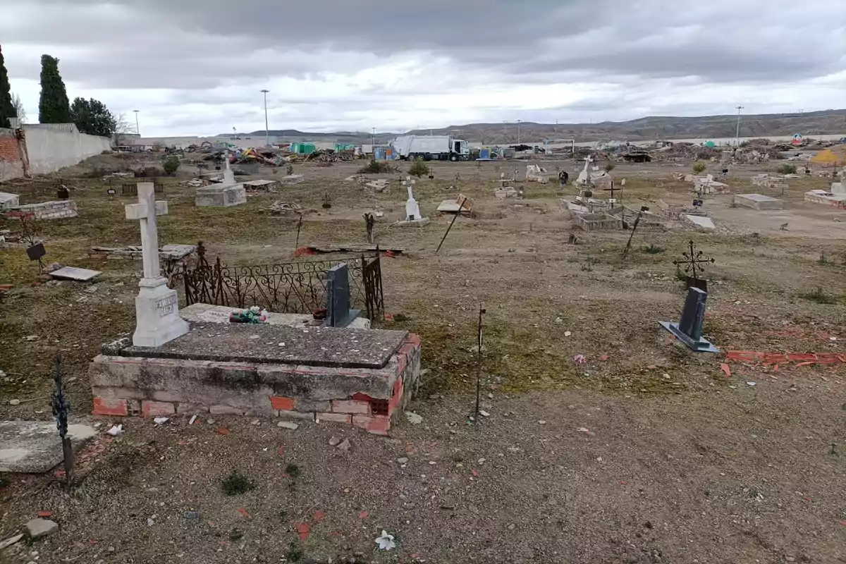 Un cementerio con tumbas dispersas y un cielo nublado en el fondo.