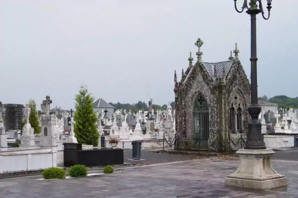 Un cementerio con tumbas y un mausoleo antiguo rodeado de lápidas y un farol en primer plano.