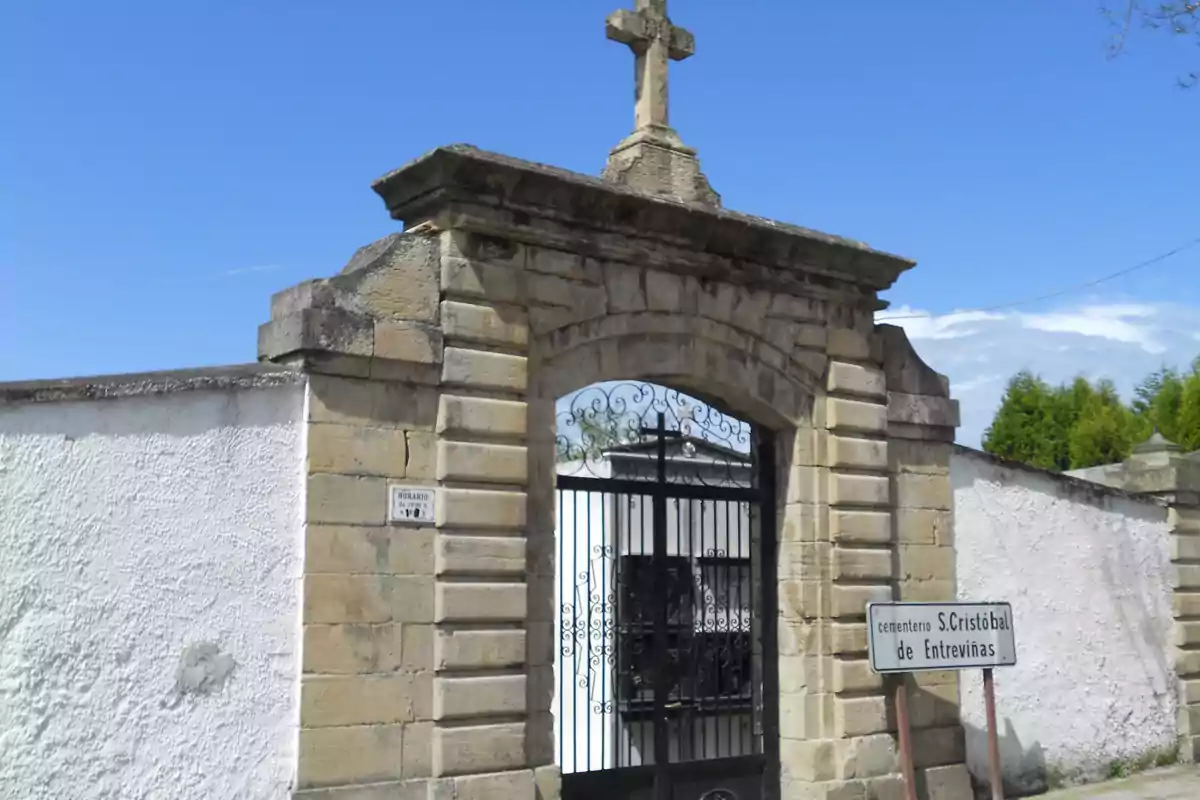 Entrada de un cementerio con una cruz de piedra en la parte superior y un cartel que indica "cementerio S. Cristóbal de Entreviñas".