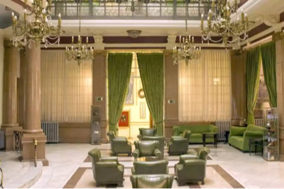Un elegante salón con columnas de mármol, cortinas verdes, lámparas de araña y sillones de cuero verde.