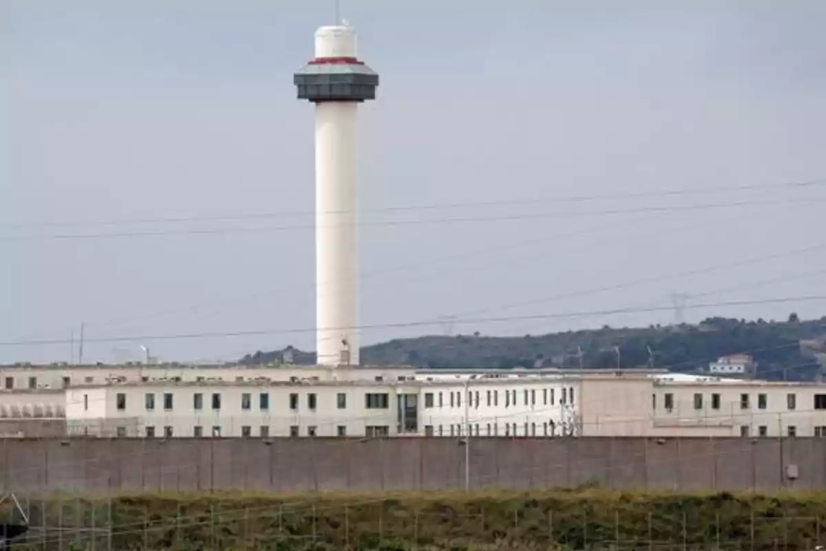 Vista de una prisión con una torre de vigilancia alta en el centro y edificios rodeados por una cerca.