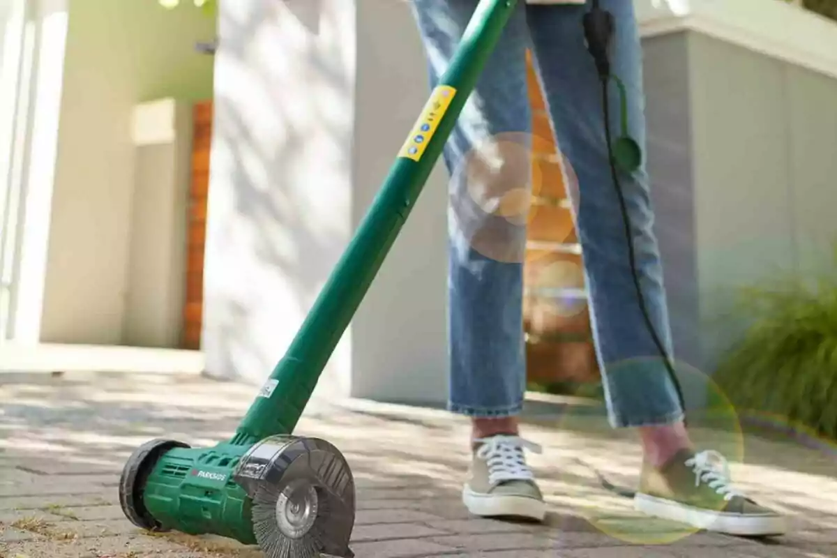 Una persona usando una herramienta eléctrica de jardinería con un cepillo giratorio en un camino pavimentado. Una persona usando una herramienta eléctrica de jardinería con un cepillo giratorio en un camino pavimentado.