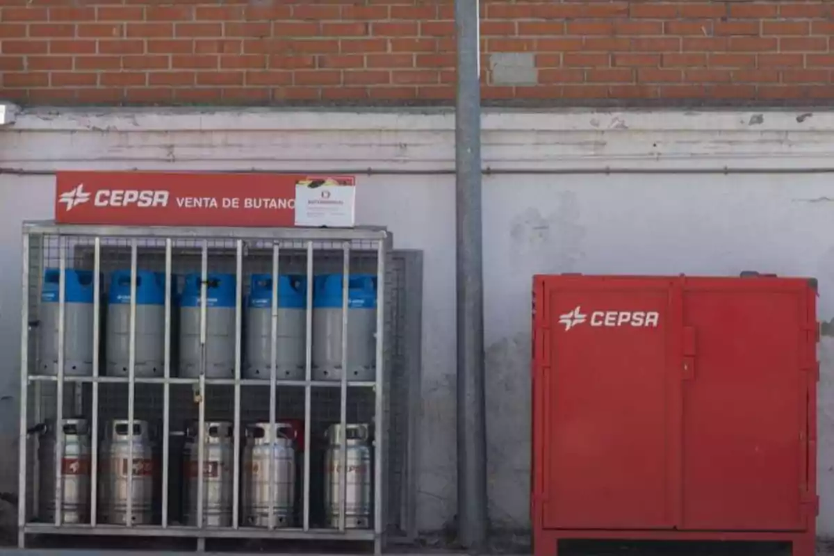 Venta de butano de CEPSA con cilindros de gas almacenados en una jaula metálica y un contenedor rojo al lado.