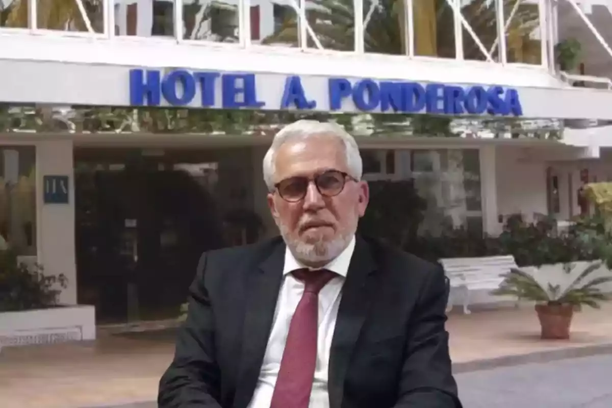 Un hombre con traje y corbata está sentado frente a la entrada de un hotel llamado Un hombre con traje y corbata está sentado frente a la entrada de un hotel llamado