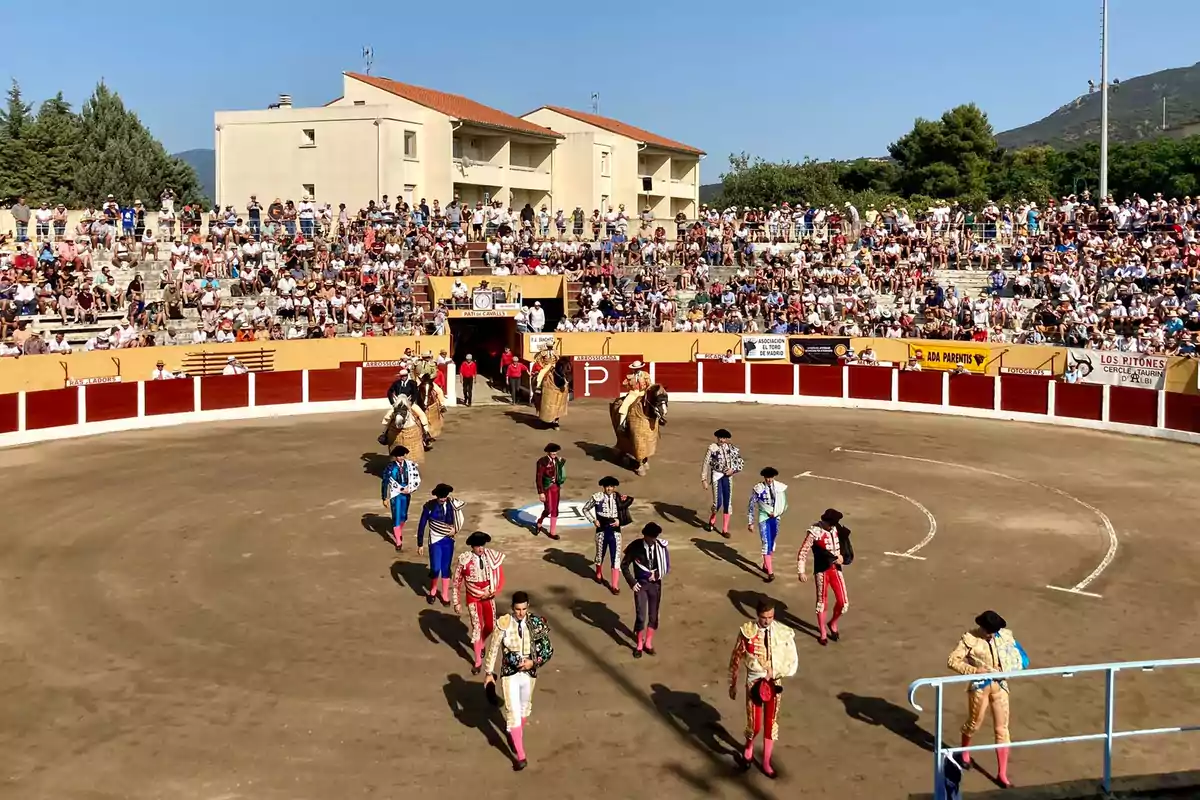 Una plaza de toros llena de espectadores, con toreros y picadores desfilando en el ruedo bajo un cielo despejado.