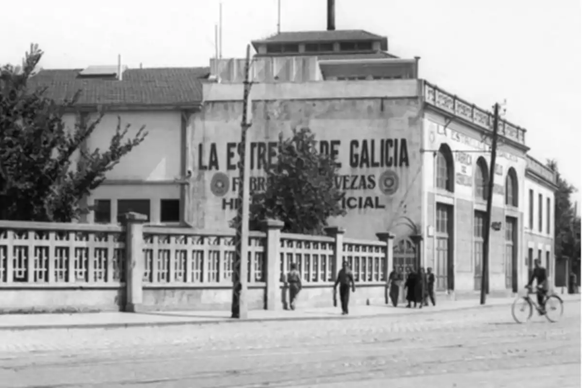 Fábrica de cervezas La Estrella de Galicia con personas caminando y un ciclista en la calle.