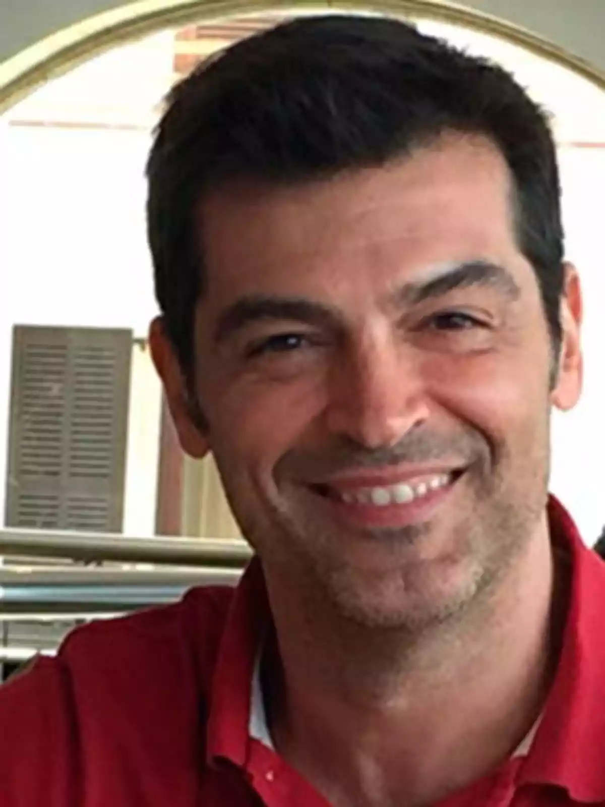 Hombre sonriendo con camisa roja en un entorno interior.