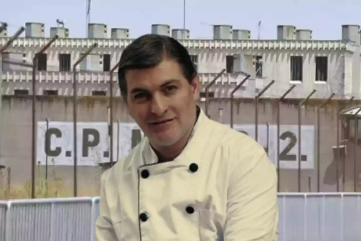 Hombre con chaqueta de chef posando frente a un edificio con rejas y un letrero que dice C.P.