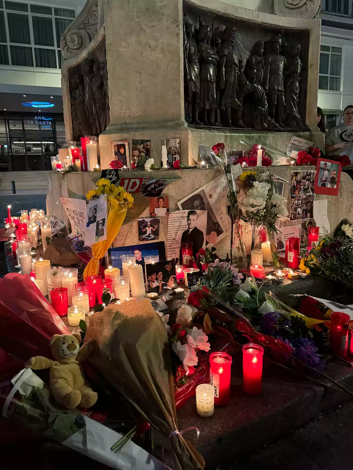 Un altar con velas, flores y fotos en homenaje a una persona frente a un monumento.