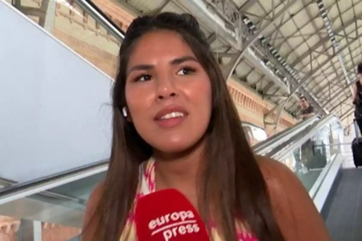 Una mujer con un micrófono de Europa Press en una estación de tren.