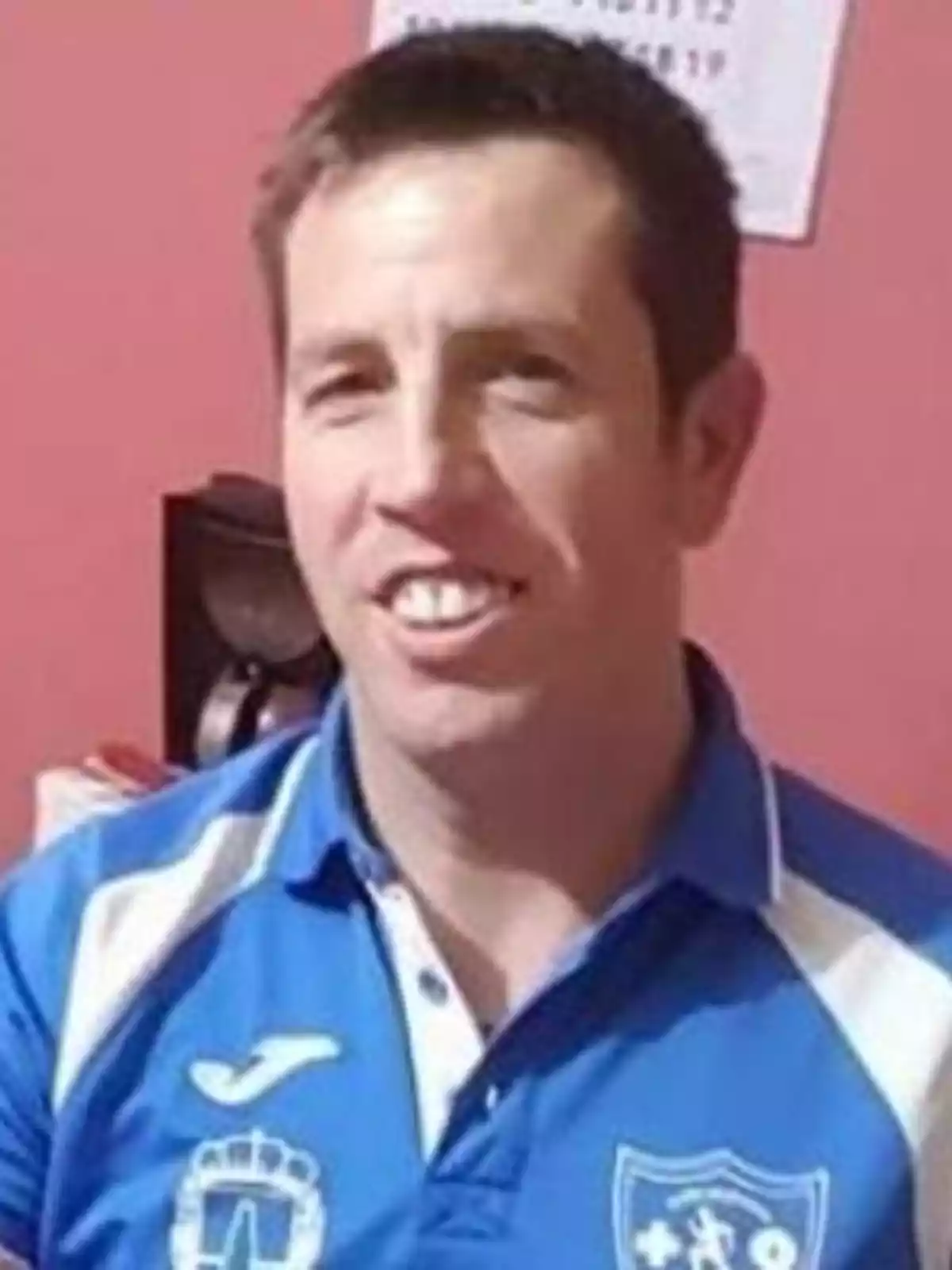 Hombre sonriendo con camiseta azul y blanca de un equipo deportivo.