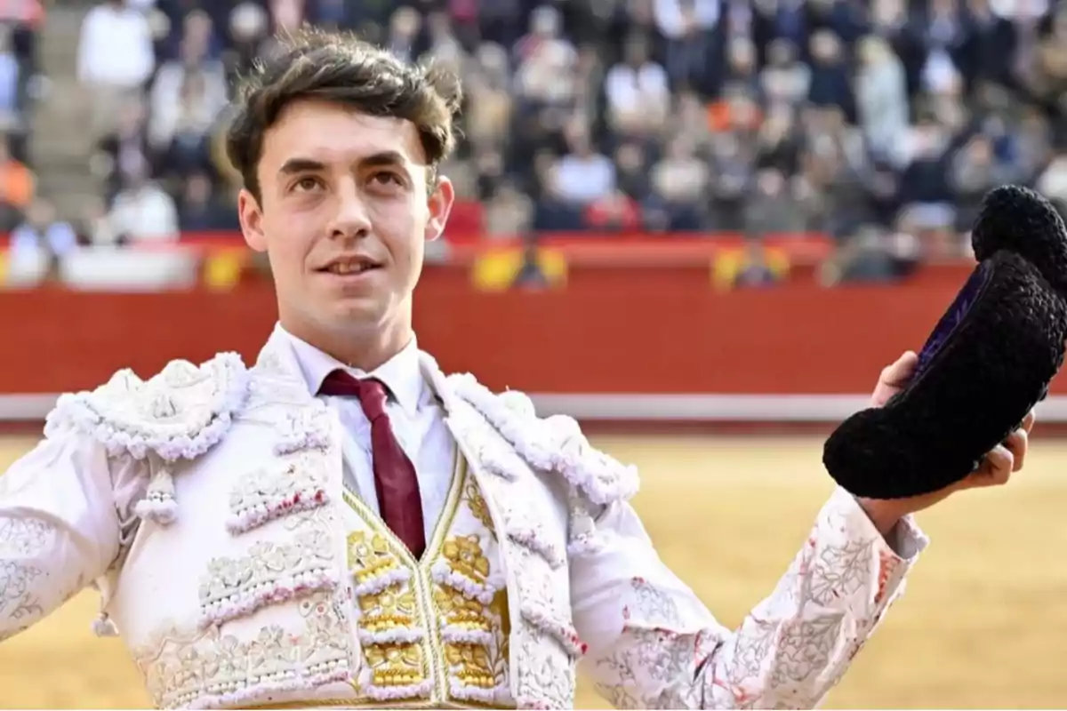 Un torero en la plaza de toros sosteniendo su montera y sonriendo al público.