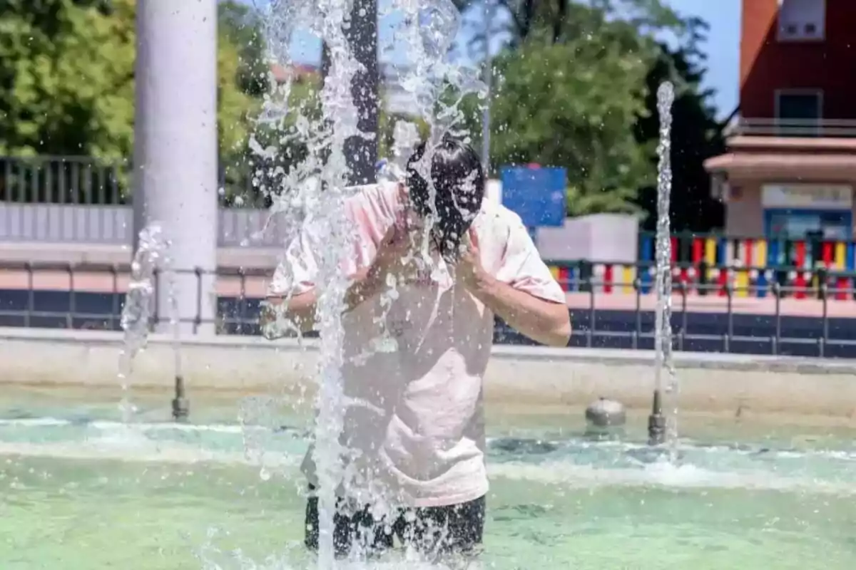 Persona refrescándose en una fuente de agua en un día soleado.