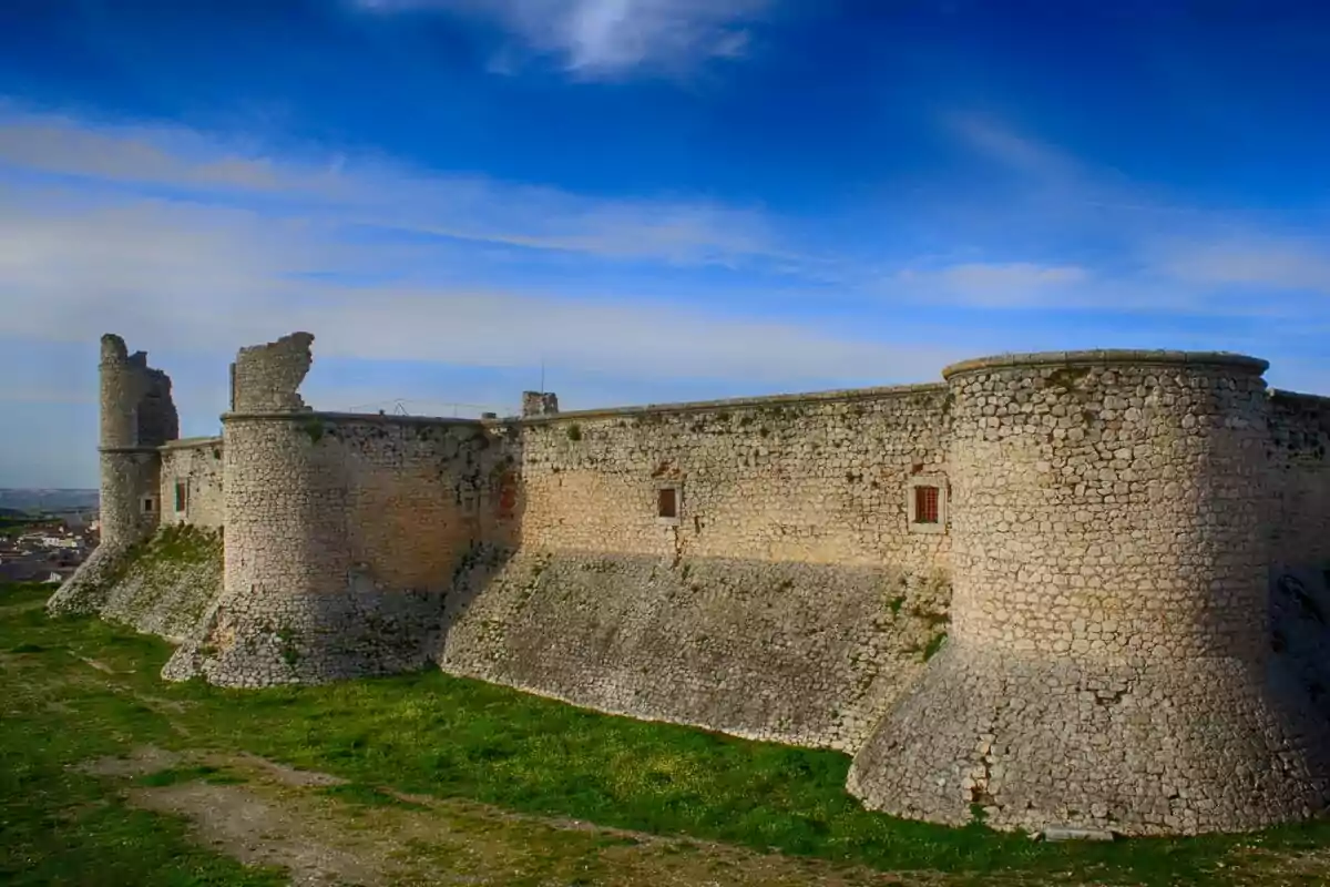 Una fortaleza de piedra antigua con torres y muros parcialmente en ruinas bajo un cielo azul. Una fortaleza de piedra antigua con torres y muros parcialmente en ruinas bajo un cielo azul.