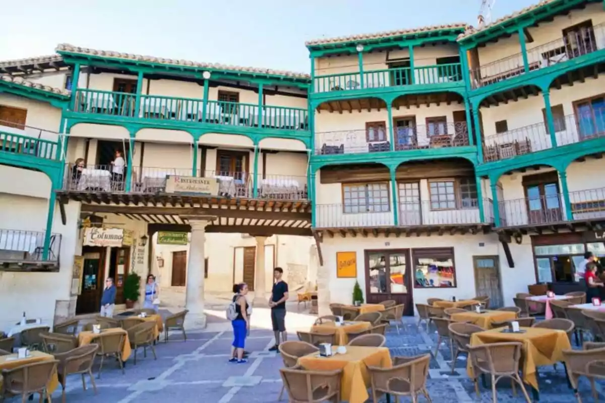 Una plaza pintoresca con edificios de balcones verdes y mesas al aire libre. Una plaza pintoresca con edificios de balcones verdes y mesas al aire libre.