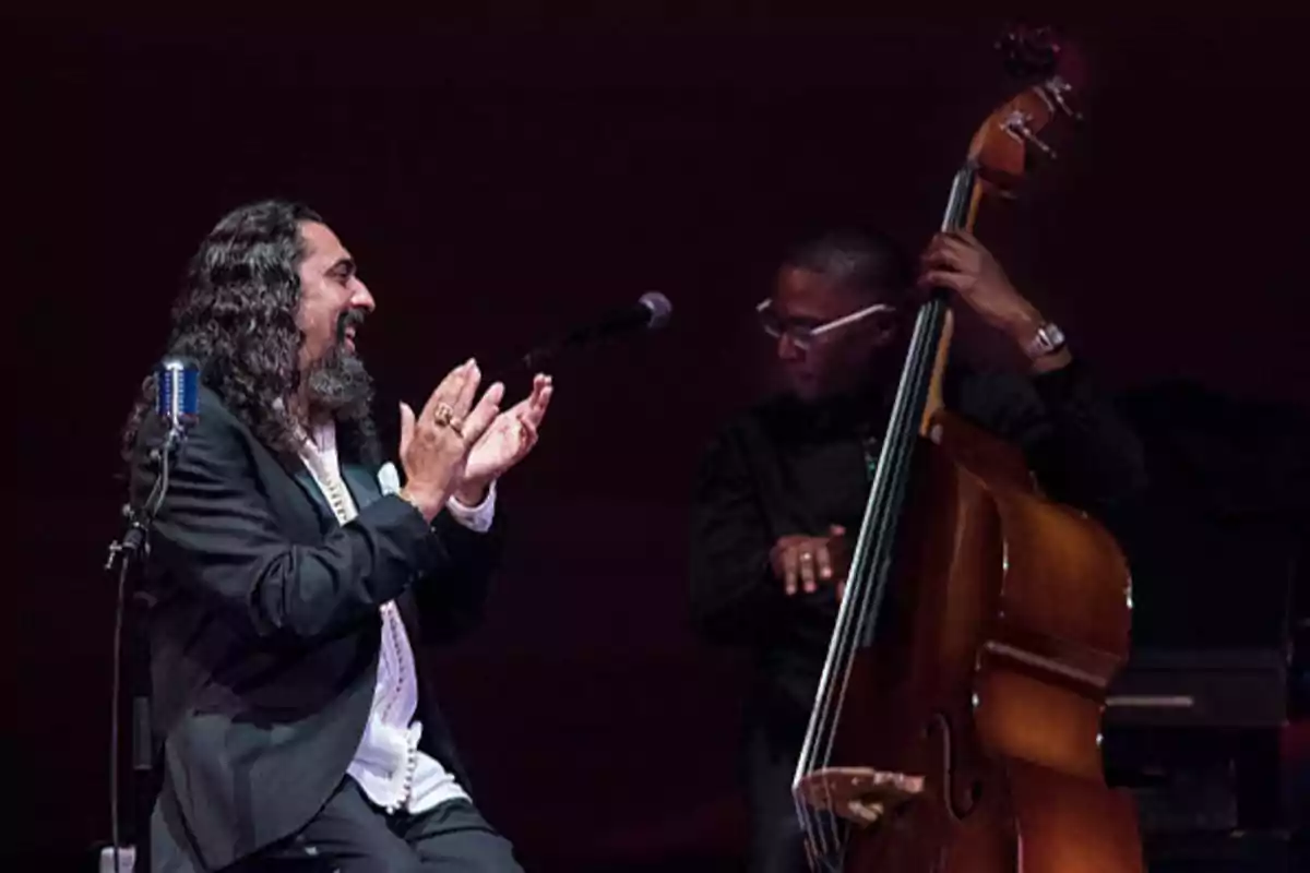 Dos músicos en el escenario, uno aplaudiendo y otro tocando un contrabajo.