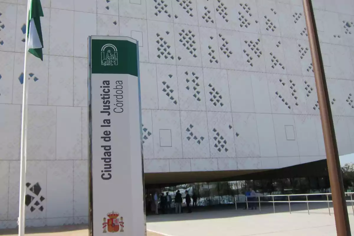 Entrada principal de la Ciudad de la Justicia en Córdoba, con un letrero vertical y una bandera ondeando a la izquierda.