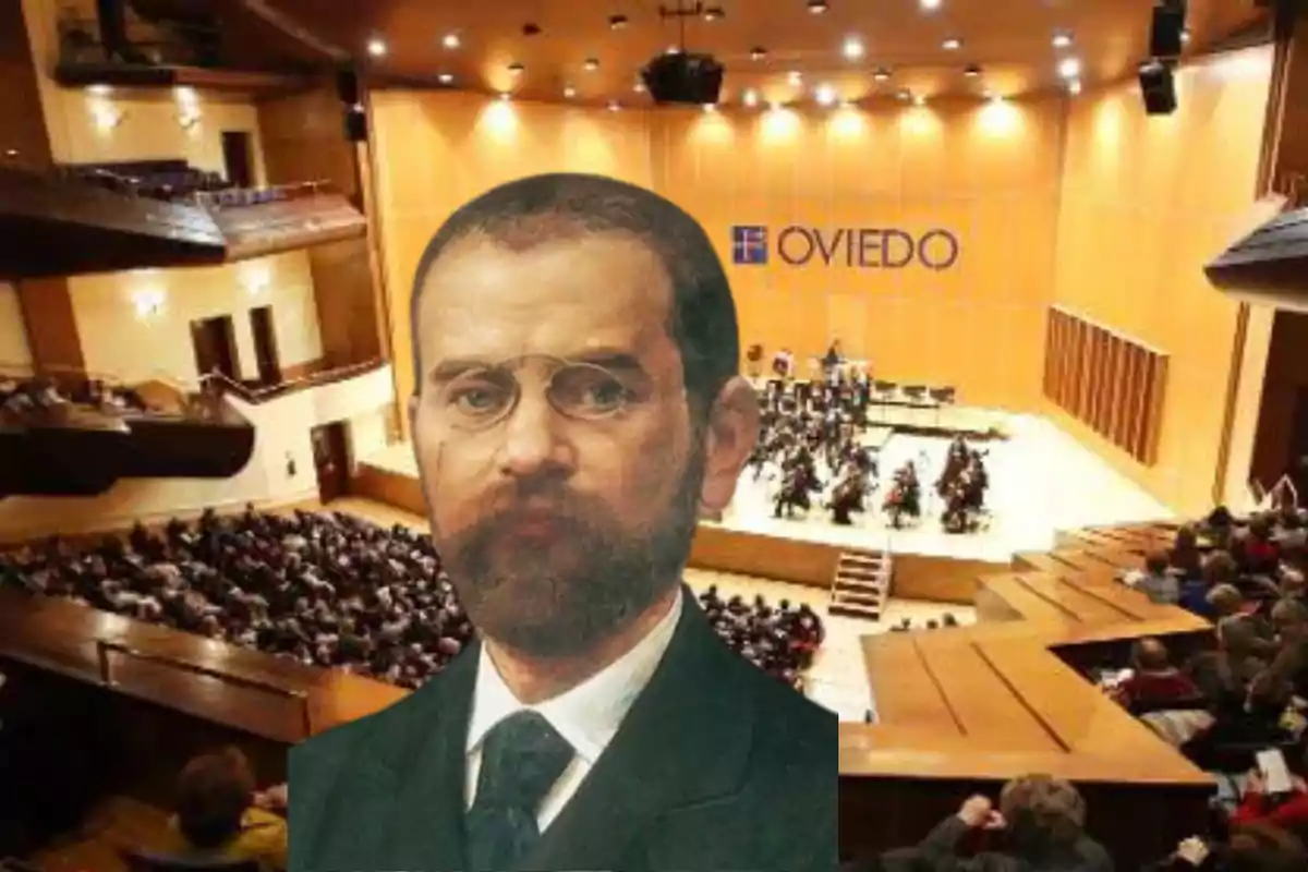 Un retrato de un hombre con gafas superpuesto sobre una imagen de un auditorio lleno de gente y una orquesta en el escenario con la palabra "Oviedo" en el fondo.