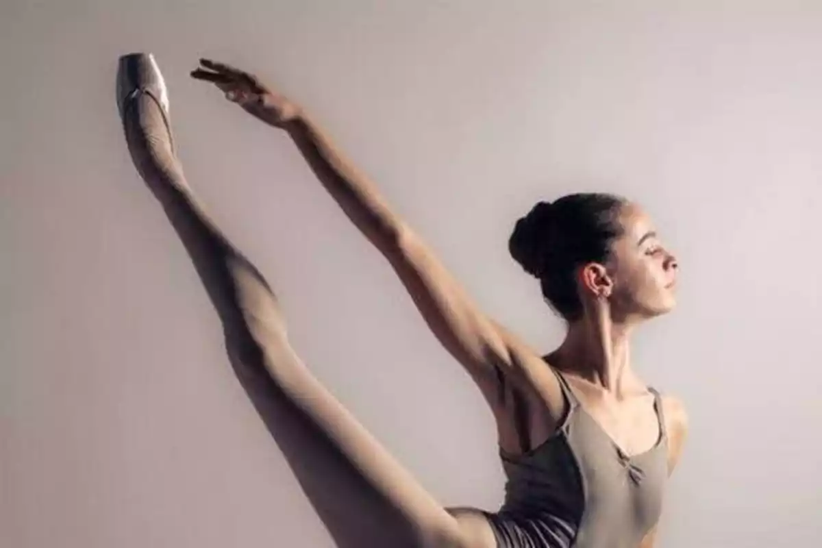 Una bailarina de ballet ejecuta una pose con una pierna levantada y un brazo extendido, mostrando su flexibilidad y gracia.