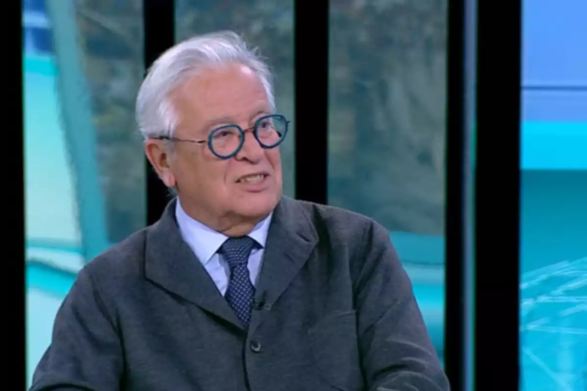 Un hombre mayor con gafas y cabello canoso está sentado en un estudio de televisión. Un hombre mayor con gafas y cabello canoso está sentado en un estudio de televisión.