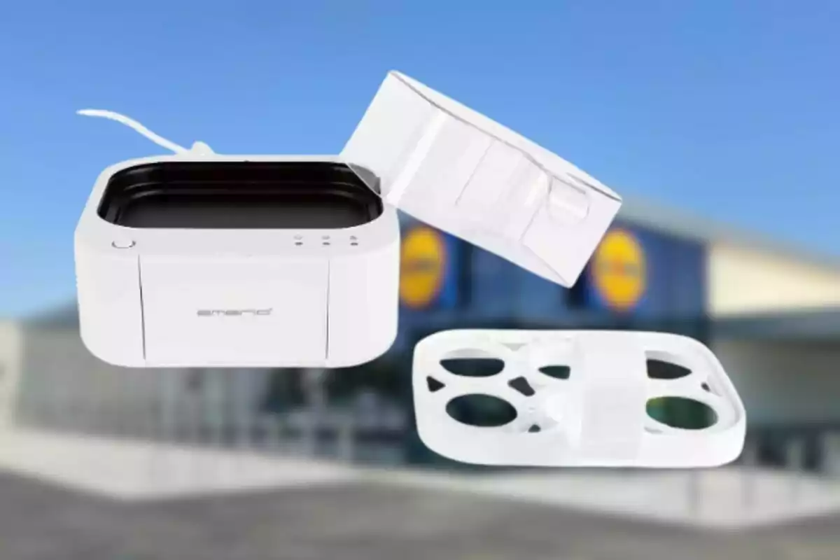 Una máquina para hacer gofres de color blanco con tapa abierta y moldes visibles, con un fondo desenfocado de un edificio. Una máquina para hacer gofres de color blanco con tapa abierta y moldes visibles, con un fondo desenfocado de un edificio.
