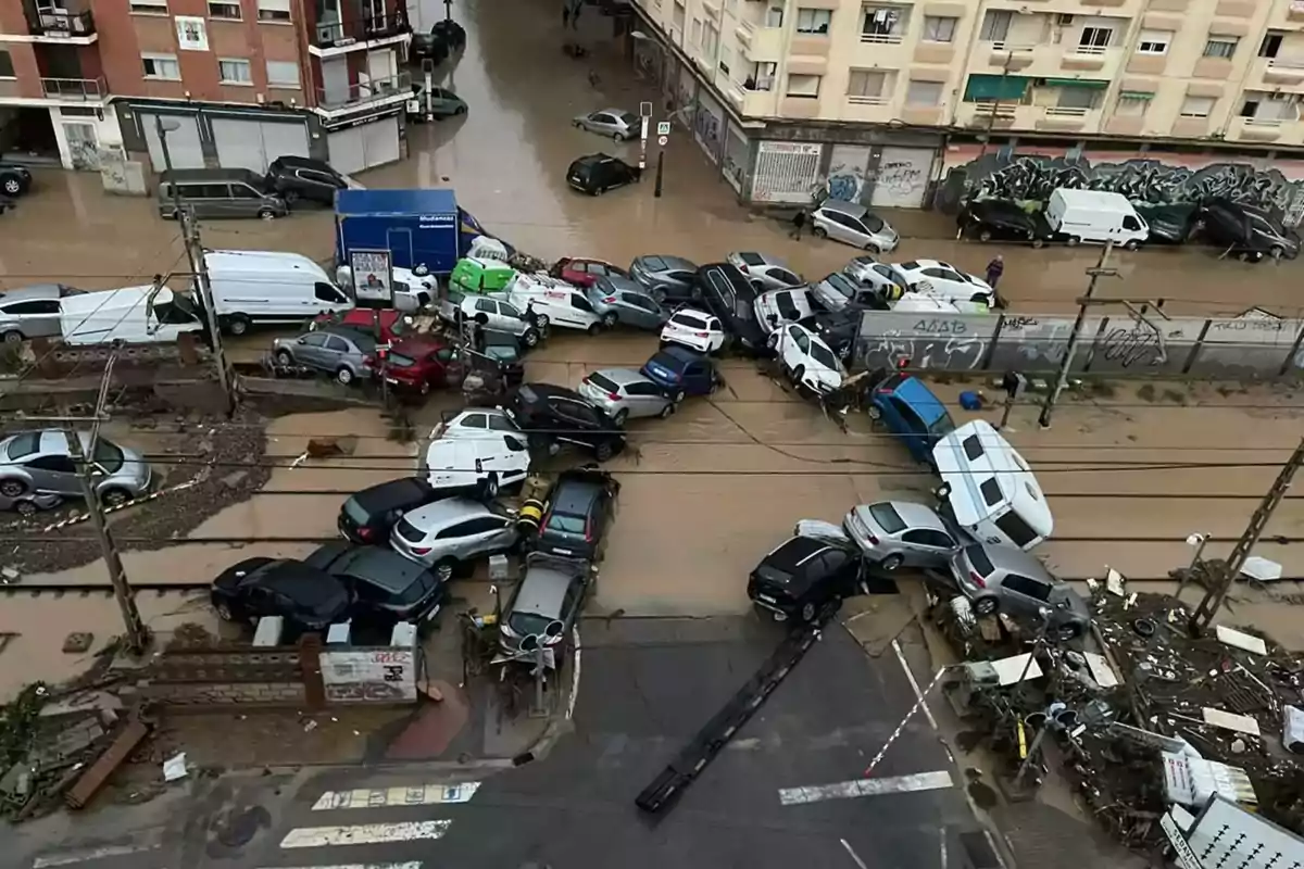 Coches amontonados y dañados en una calle inundada tras una fuerte tormenta en una zona urbana.