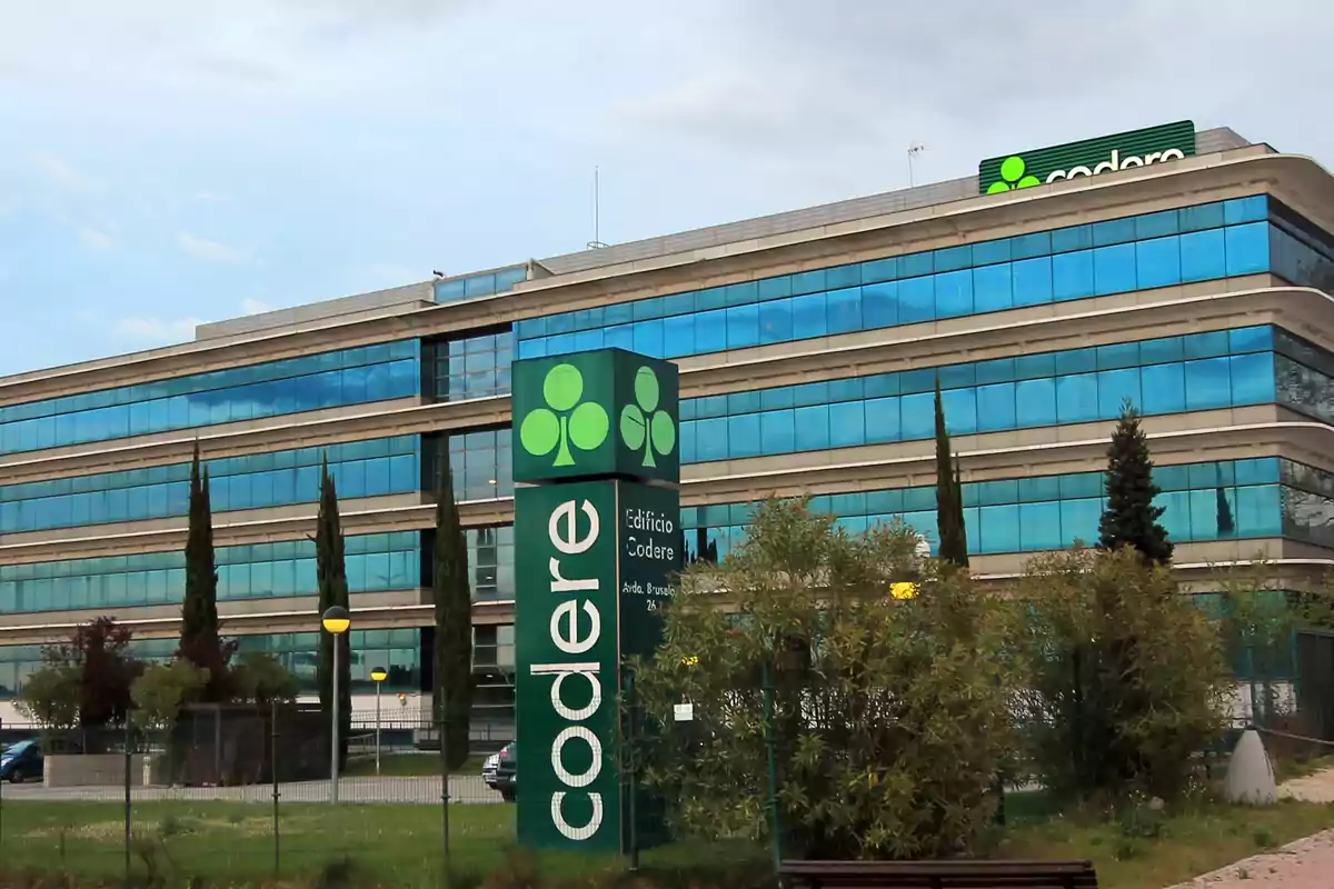 Edificio de oficinas con fachada de vidrio azul y un letrero verde que dice 