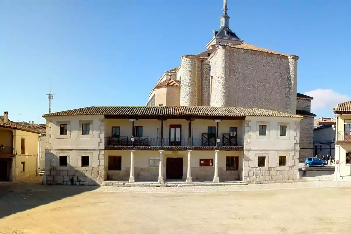 Edificio histórico con fachada de piedra y balcones de madera frente a una plaza abierta bajo un cielo despejado.