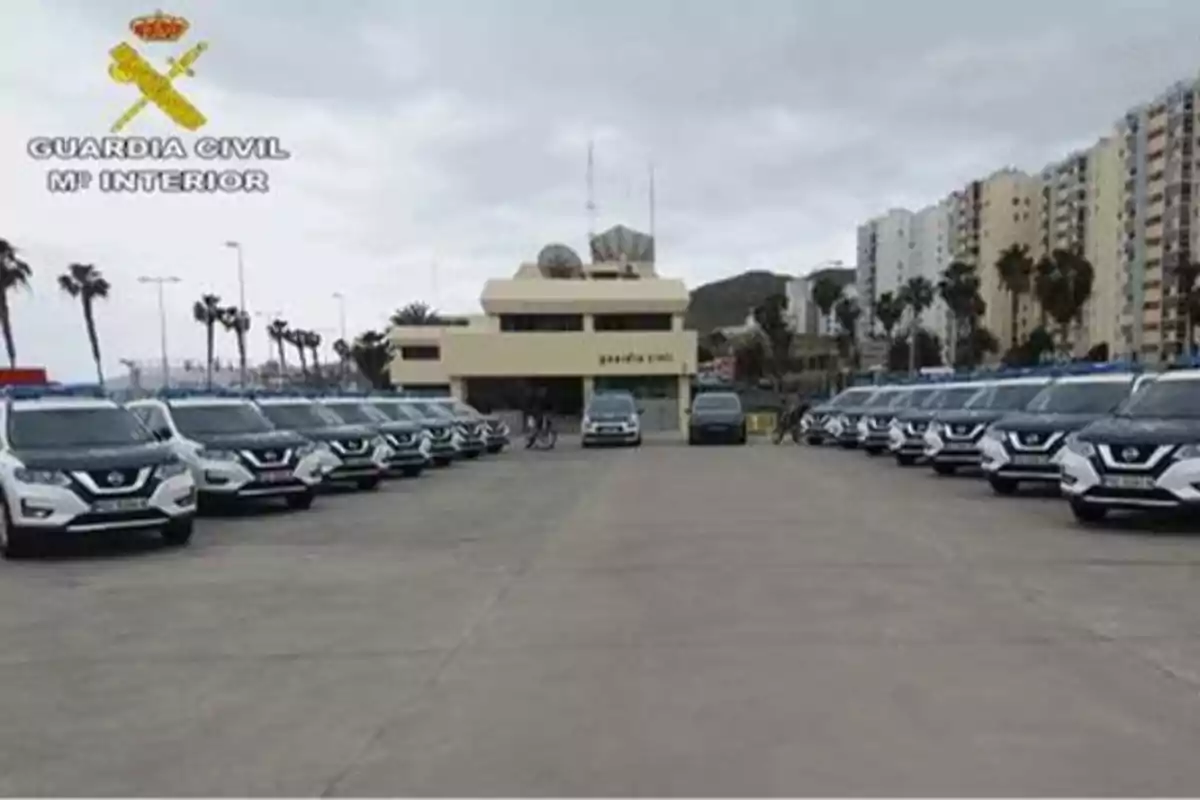 Una flota de vehículos de la Guardia Civil estacionados frente a un edificio oficial con el logotipo de la Guardia Civil y el Ministerio del Interior en la esquina superior izquierda.