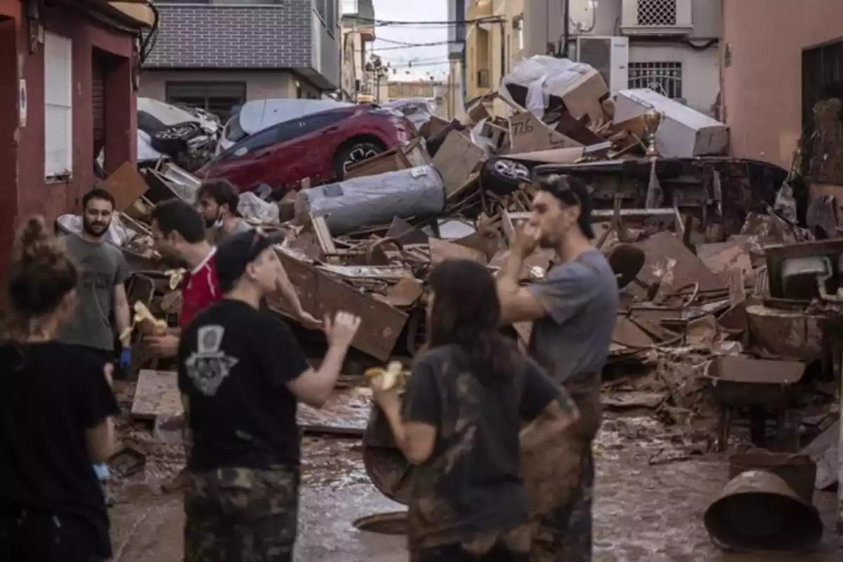 Personas observan una calle llena de escombros y vehículos dañados tras una inundación.