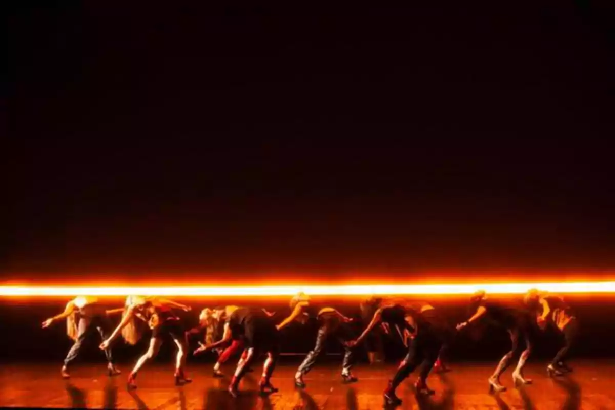 Un grupo de bailarines en el escenario iluminado por una línea de luz naranja en el fondo.