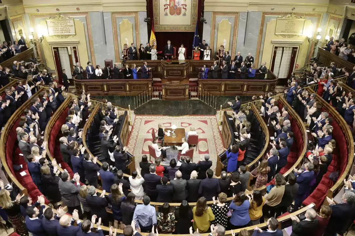 Una sesión parlamentaria con numerosos asistentes aplaudiendo en un hemiciclo.
