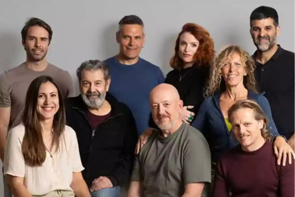Grupo de ocho personas adultas posando juntas y sonriendo frente a un fondo gris Grupo de ocho personas adultas posando juntas y sonriendo frente a un fondo gris