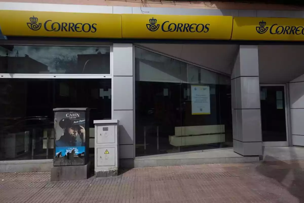 Fachada de una oficina de Correos con un cartel publicitario en la acera. Fachada de una oficina de Correos con un cartel publicitario en la acera.