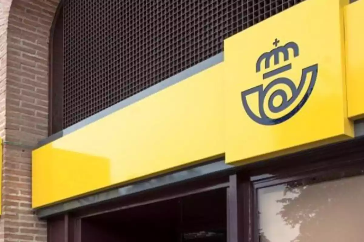 Fachada de una oficina de correos con un cartel amarillo y un logotipo negro. Fachada de una oficina de correos con un cartel amarillo y un logotipo negro.