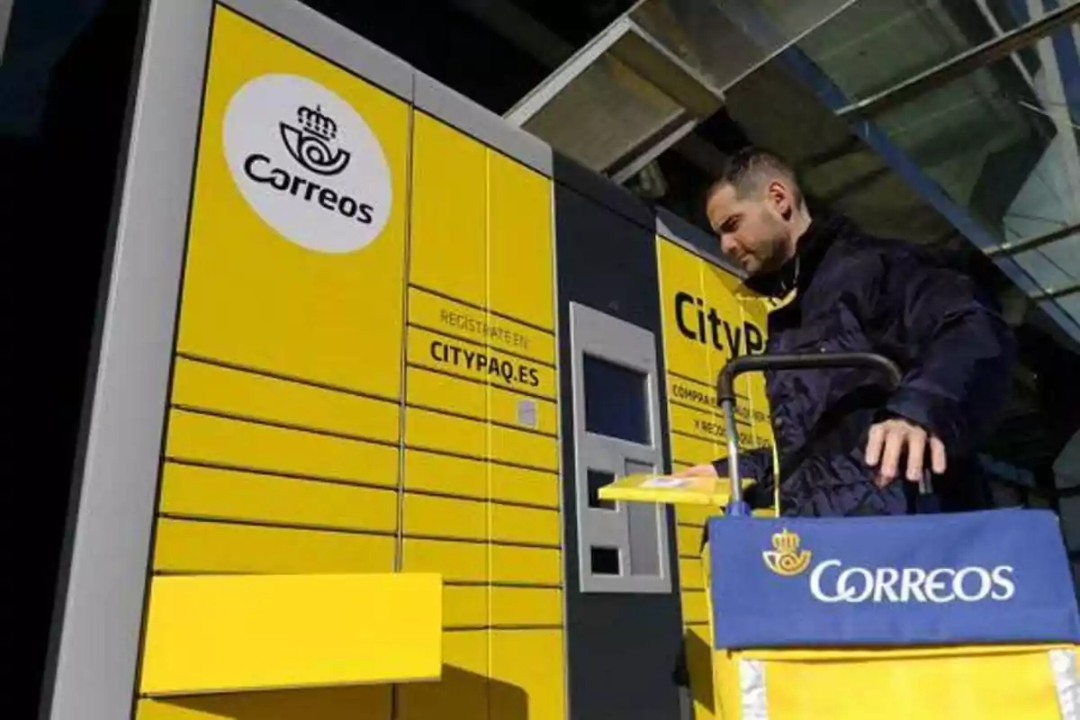 Un hombre utilizando un terminal de paquetería de Correos con un carrito de reparto.