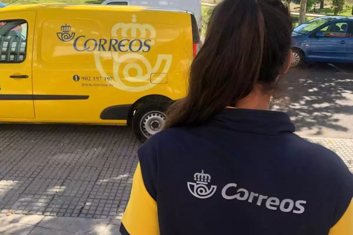 Persona de espaldas con uniforme de Correos frente a una furgoneta amarilla de la misma empresa estacionada en la calle.