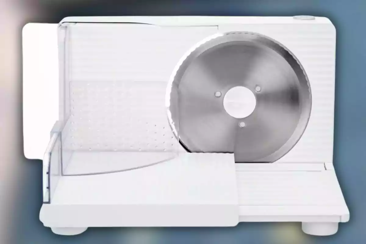 Una rebanadora de alimentos eléctrica con una cuchilla circular de acero inoxidable y una base blanca.
