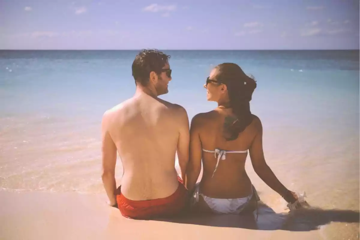 Una pareja sentada en la orilla de la playa mirando el mar.