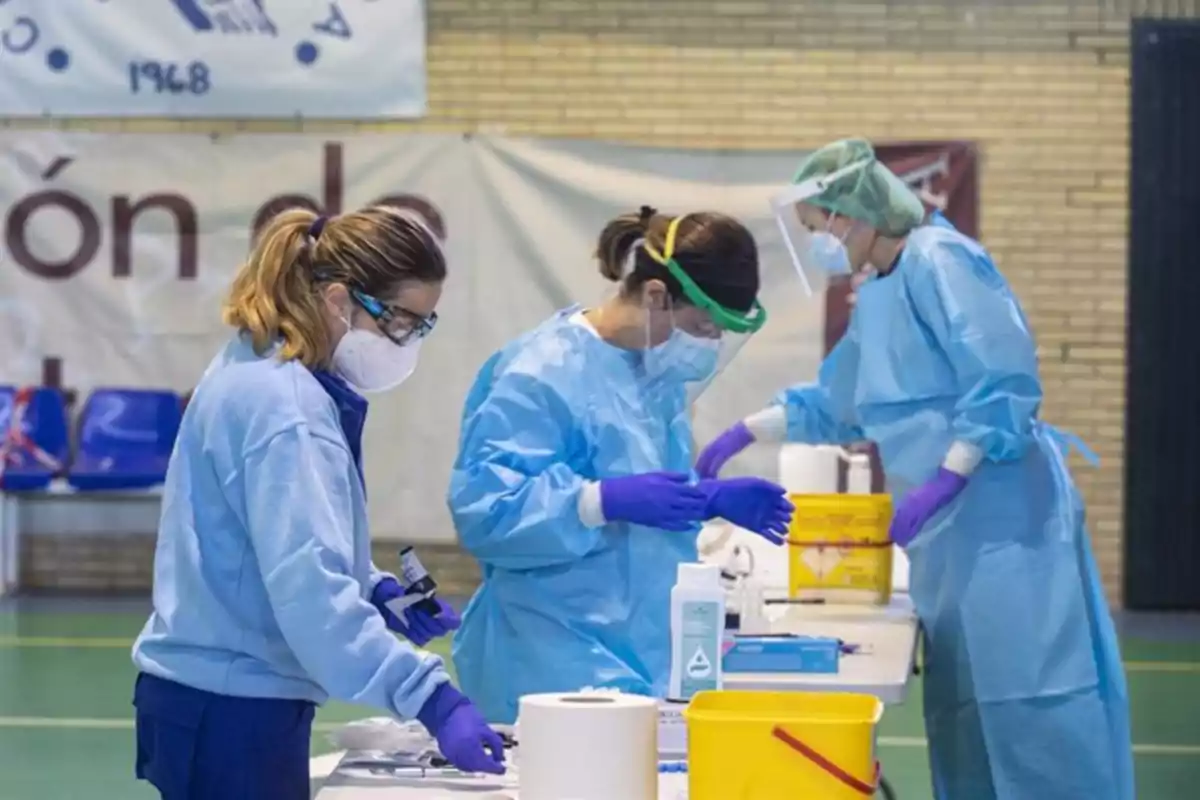 Personal médico con equipo de protección realiza pruebas en una mesa dentro de un recinto cerrado