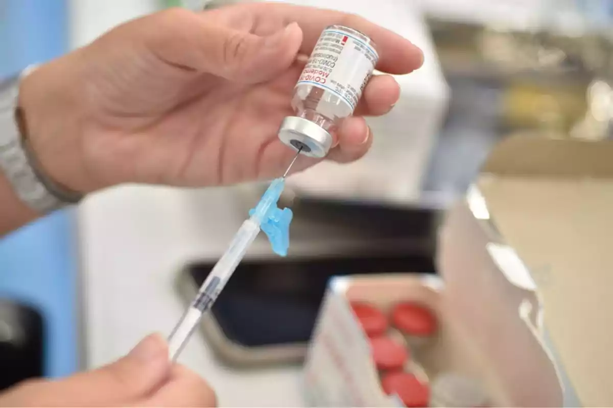 Mano sosteniendo un vial de vacuna mientras una jeringa está siendo llenada con el líquido.